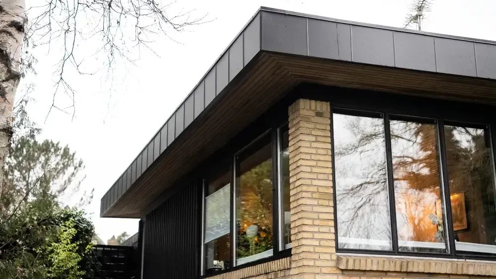 Murstensfacade med mørk beklædning og træunderside